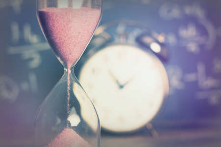 Hourglass against on wooden surface with a blackboard backgroundの写真素材