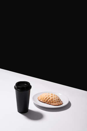 Freshly baked armadillo Mexican artisan bread on a white plate on a white table and a black wall in the background with a black cup of coffee, no peopleの写真素材