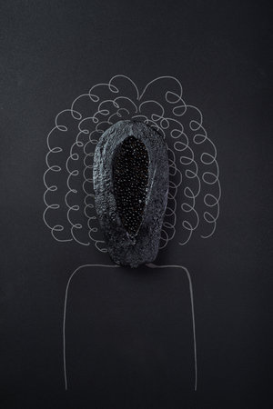 a black painted papaya cut in half on a solid black background and the silhouette of a woman with curly hair, concept of female health, healthy vagina, no peopleの写真素材