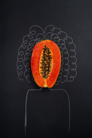 a papaya cut in half on a solid black background and the silhouette of a woman with curly hair, concept of female health, healthy vagina, no peopleの写真素材