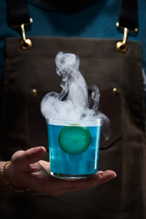 Special mixology cocktail, rum with curacao, blue color, lemon and hydrogen, man with apron holds the drink, closed upの写真素材
