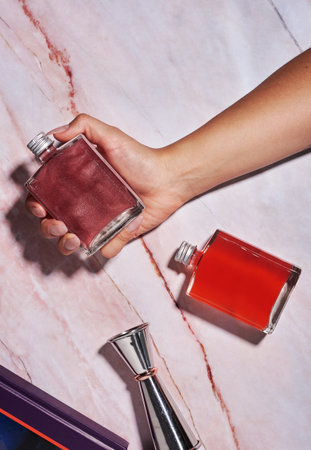 a woman's hand has two glass jars with rum cocktails, gin, Cosmopolitan style, hard light on an ivory table with bar items, one handの写真素材
