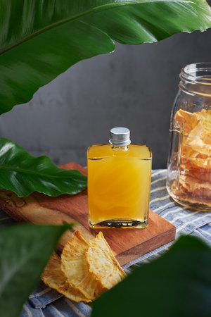 Glass jar with special cocktail of pineapple, rum and mezcal with garnish chili and pineapple plants garnished with dried fruit in a kitchen with plants, no peopleの写真素材