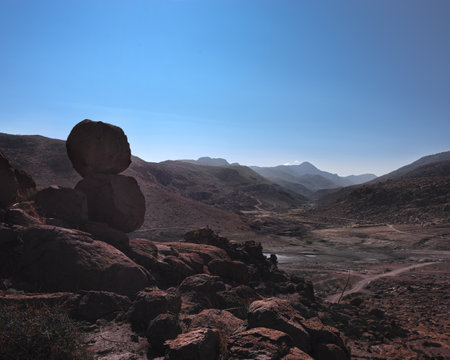 mountain top with plains in the background, two rocks stacked on top of a stone mountain, a road path in the distance, mountainous summer landscape without people, beautiful viewの写真素材