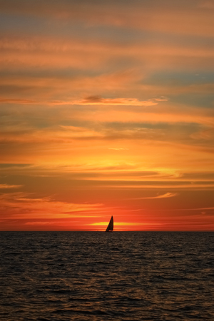 Lonely yacht far on the horizon sailing at sunset with spectacular orange clouds.の写真素材