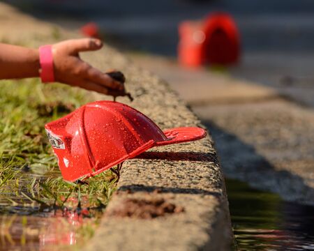 Shiny red fireman's hat held by a child's hand in the rain.