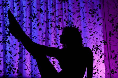 Woman doing yoga in a silhouette against a purple backgroundの写真素材