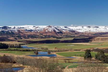 Snow covered mountains behind valleys and field with dams of waterの写真素材