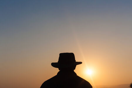Man unidentified wearing hat body outline contrasts silhouetted at sun setting late afternoonの写真素材