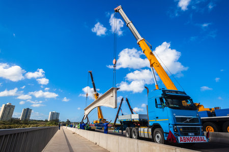 Construction heavy civil engineering rigging of large concrete bridge section lifted off truck and installed by two cranes のeditorial素材