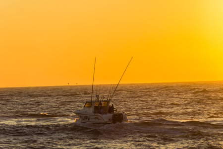 Fishing boat heads out to sea while the sun rises creating an orange sky のeditorial素材