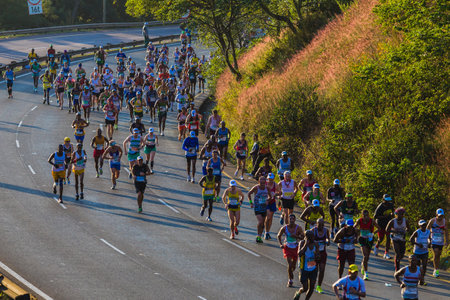 Marathon ultra distance race with groups of runners up long winding hill in morning sun lightのeditorial素材