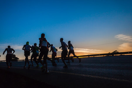 Marathon ultra race with groups of runners up long winding hill silhouetted in morning sun lightのeditorial素材