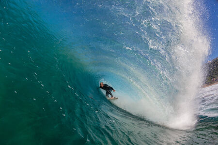 Surfer tube rides inside hollow crashing blue clean smooth shape ocean wave over shallow reefsの写真素材