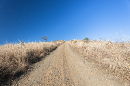 Steep dirt road upwards , four wheeler terrain into the blue sky with dry rural wild countryside  landscapeの写真素材