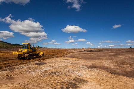 Breaking new ground, farmland conversion for industrial construction of warehouse buildings in rural countryside with earth grading machines on bare soil in blue sky landscapeの写真素材