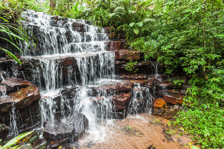 Small rock waterfall in rural countryside with clean clear water flowing over terraced rocks from stream through green tree plant vegetationの写真素材