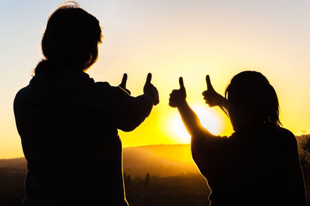 Mother daughter affections relationship love discipline contrasts silhouetted in dusk sunset skyの写真素材