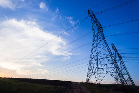 Electrical tower pylons cable power-lines silhouetted in afternoon sunset blue sky