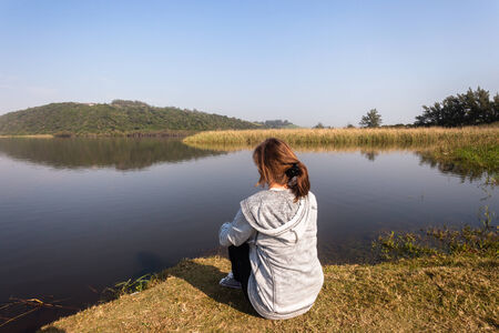 Teen girl relax sitting by beach sea river lagoon waters on a calm blue day in the countrysideの写真素材