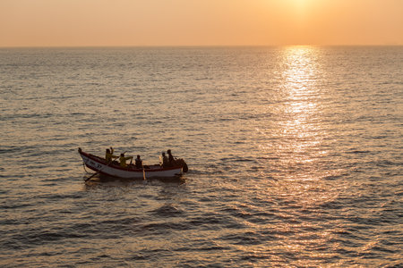Fishermen using hand paddle oars boat in sea waters about to cast sowing nets as the sun rising reflections bring a new dayのeditorial素材