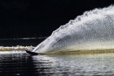 Slalom water skier turn creating upright water wall contrast in morning lightの写真素材