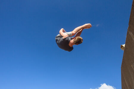 Teen boy parkour jumping off wall into summersault flips on beach