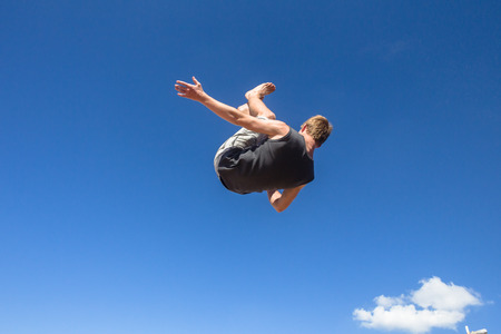 Teen boy parkour jumping off wall into summersault flips on beachの写真素材