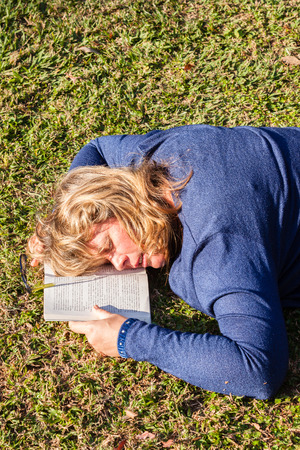 Woman at home relaxing outdoors reading book sleeping nap in afternoon sunlightの写真素材