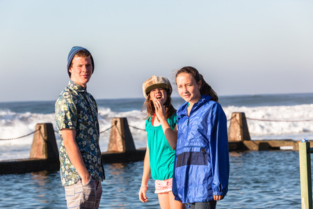Teenagers boy girls morning social talk time at beach tidal pool with ocean waves 