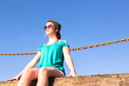 Teenager girl warms up in sunlight relaxing sitting at beach tidal pool block watching blue ocean waves holidayの写真素材