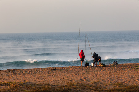 Fishermen surf fishing on beach early morning with river mist out on ocean sea wave waters の写真素材