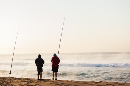 Fishermen surf fishing on beach early morning with river mist out on ocean sea wave waters の写真素材