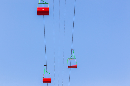 Cable lift chairs red suspened in blue sky high above groundの写真素材