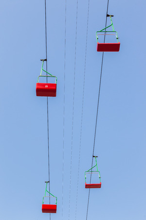 Cable car lift chairs red suspened in blue sky high above groundの写真素材
