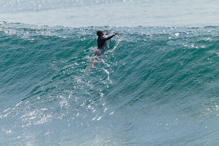Surfing surfer paddles over ocean waveの写真素材