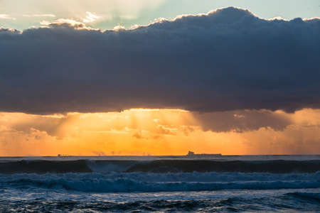 Ocean waves sunrise clouds ships silhouetted in morning color contrast on horizonの写真素材