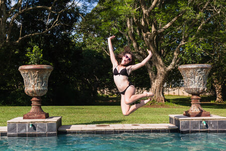 Girl Teenager jumping into swimming pool summer playtimeの写真素材