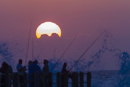 Dawn Sunrise over the ocean with fishermen on beach pir silhouettedの写真素材