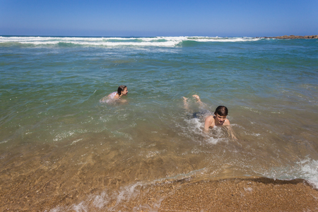 Teenager boy girl ocean swimming beach shorebreak holiday landscapeの写真素材