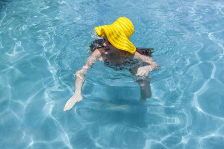 Girl swim with yellow hat home swimming pool summerの写真素材