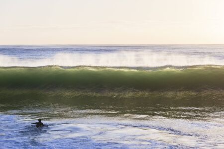 Wave ocean wall crashing front of  surfer paddling.