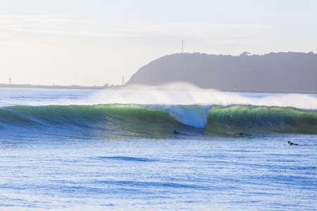 Wave  ocean wall crashing with surfers paddling.