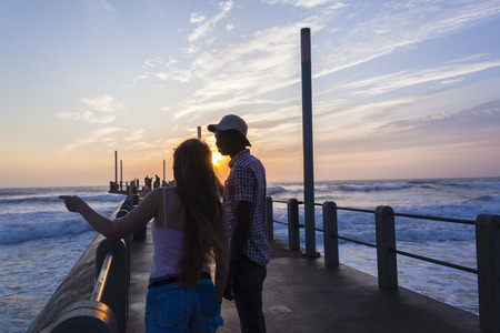 Friends man girl silhouetted talking conversation beach pier ocean sunrise lifestyleの写真素材
