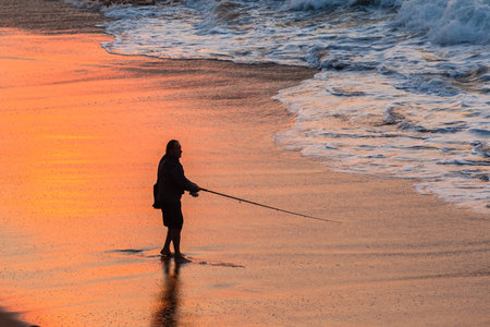 Fisherman silhouetted fishing beach waterline ocean sunrise landscapeのeditorial素材