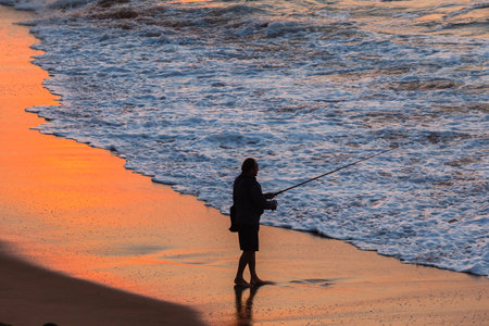 Fisherman silhouetted fishing beach waterline ocean sunrise landscapeのeditorial素材
