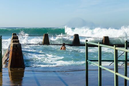 Girl in beach tidal swimming  pool chain wall with big ocean waves.の写真素材