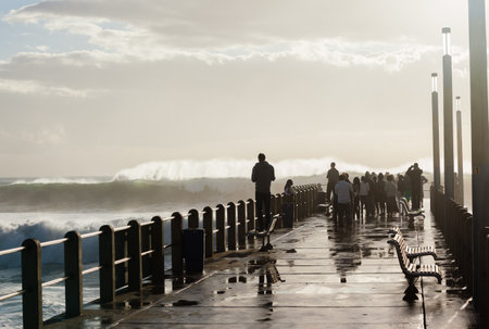 People spectators on beach piers watching storm waves crashing power of natureのeditorial素材
