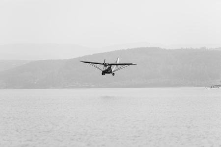 Pilot flying low in light microlight two seater plane over dam lake waters.の写真素材