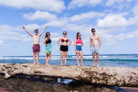 Family teenagers girls boys happy expressions beach ocean holidays standing on tree trunk.の写真素材